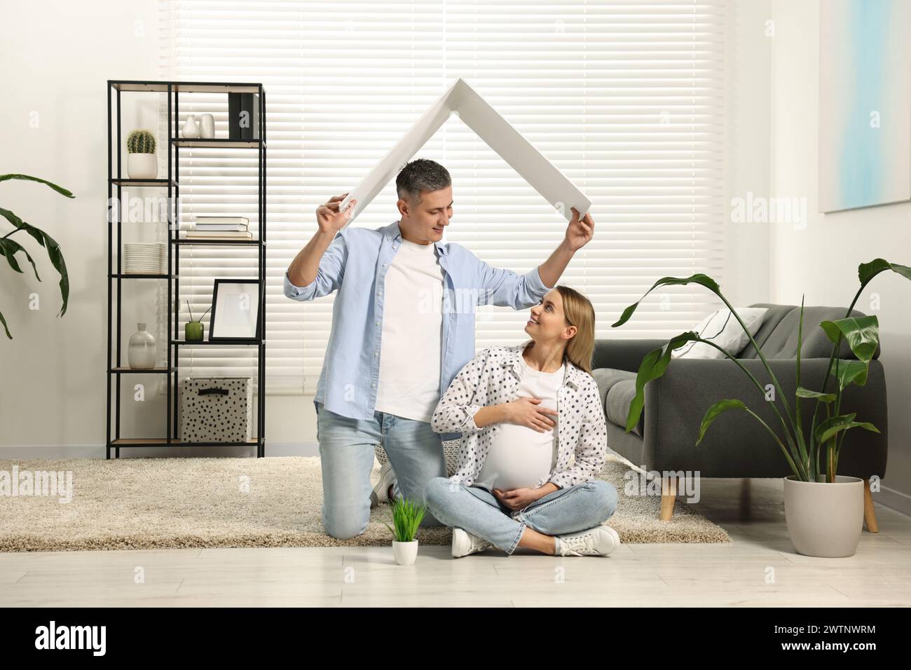 Concept de logement pour jeunes familles. Homme tenant un toit en carton au-dessus de sa femme enceinte tête à la maison Banque D'Images
