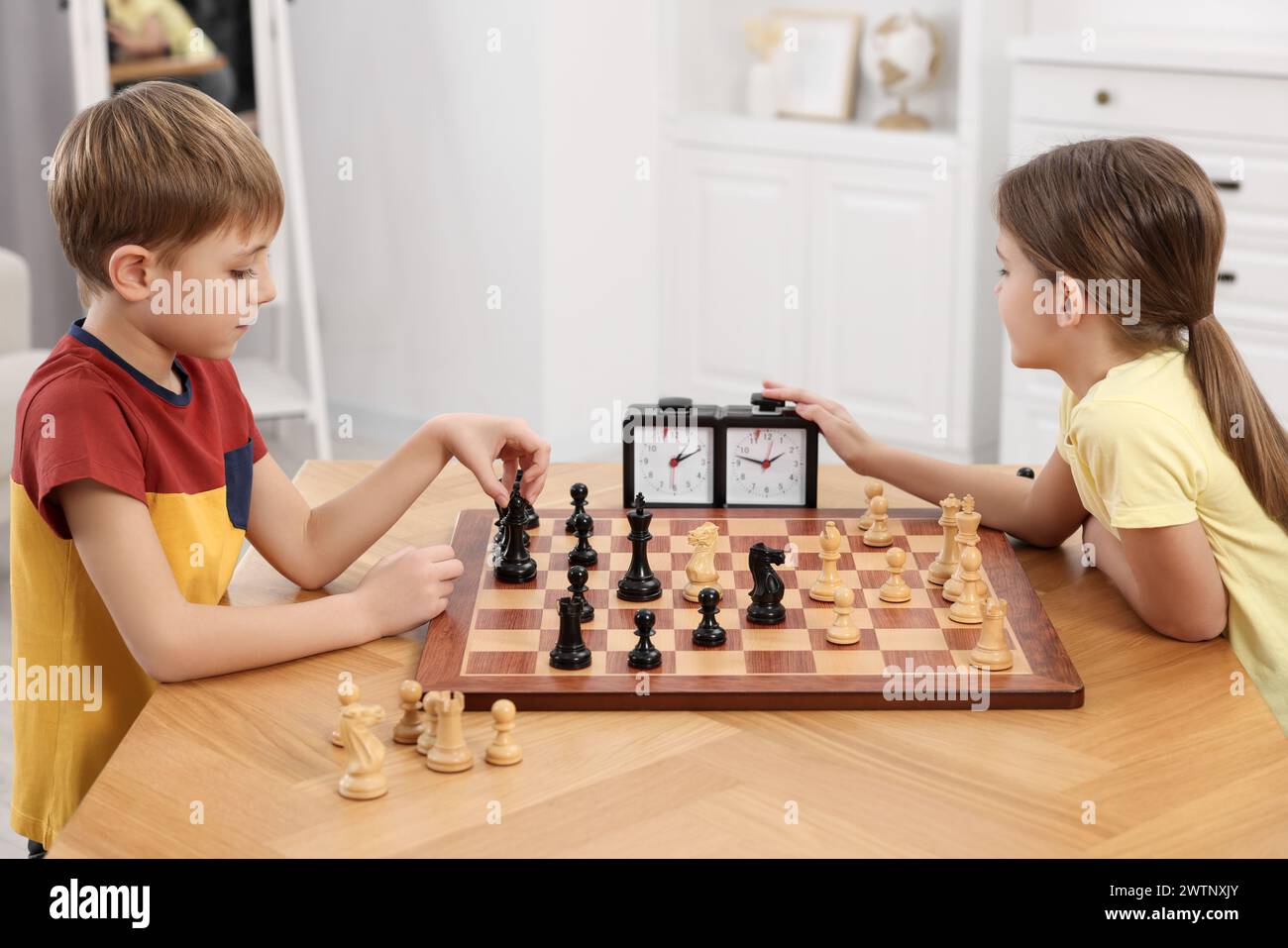 Enfants mignons jouant aux échecs à table dans la chambre Banque D'Images