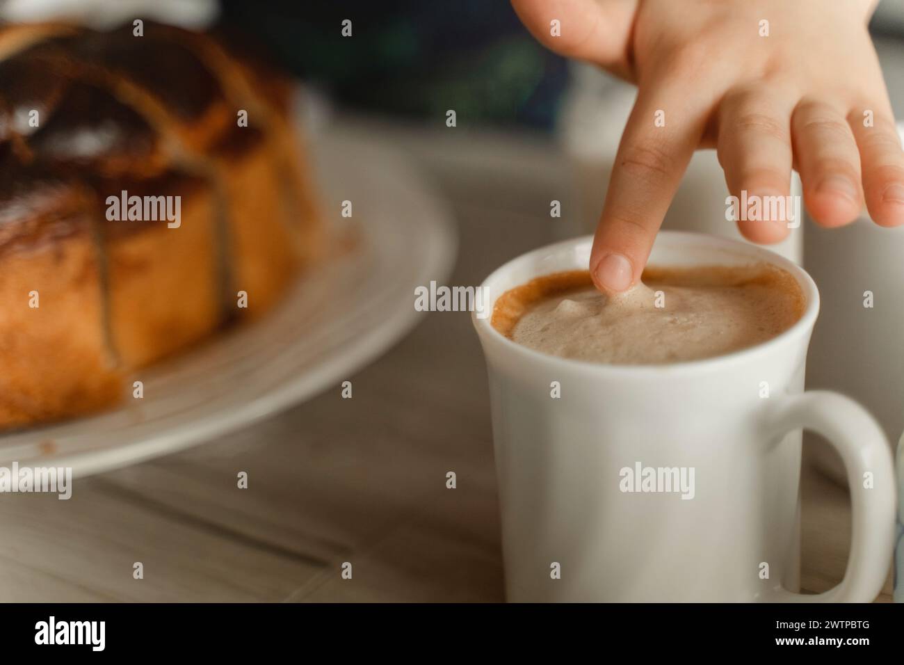 Main d'une personne tendue la main pour prendre une tasse de café chaud à la vapeur sur une table. Banque D'Images