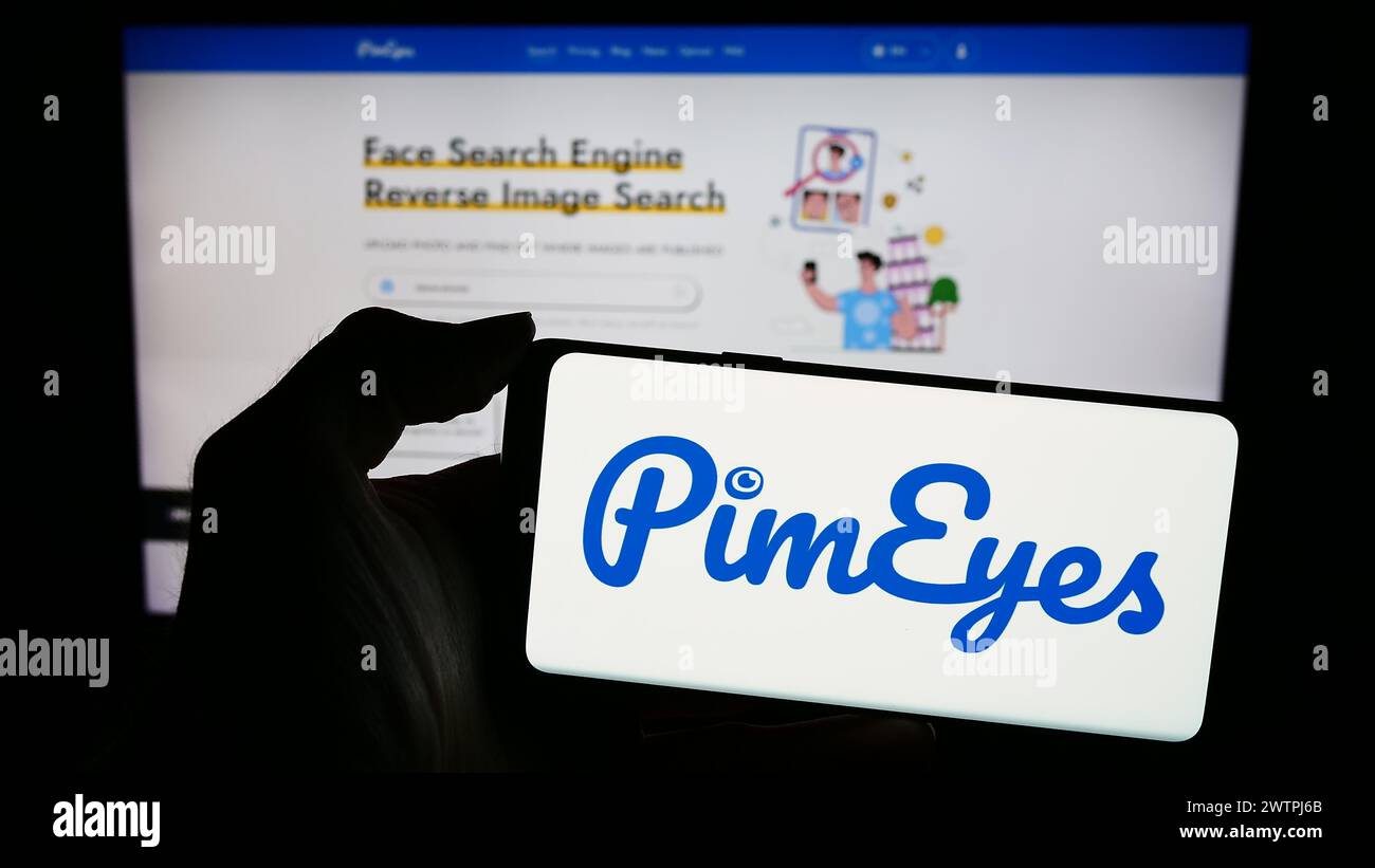Personne tenant le téléphone portable avec le logo de la société de recherche de reconnaissance faciale PimEyes en face de la page Web de l'entreprise. Concentrez-vous sur l'affichage du téléphone. Banque D'Images