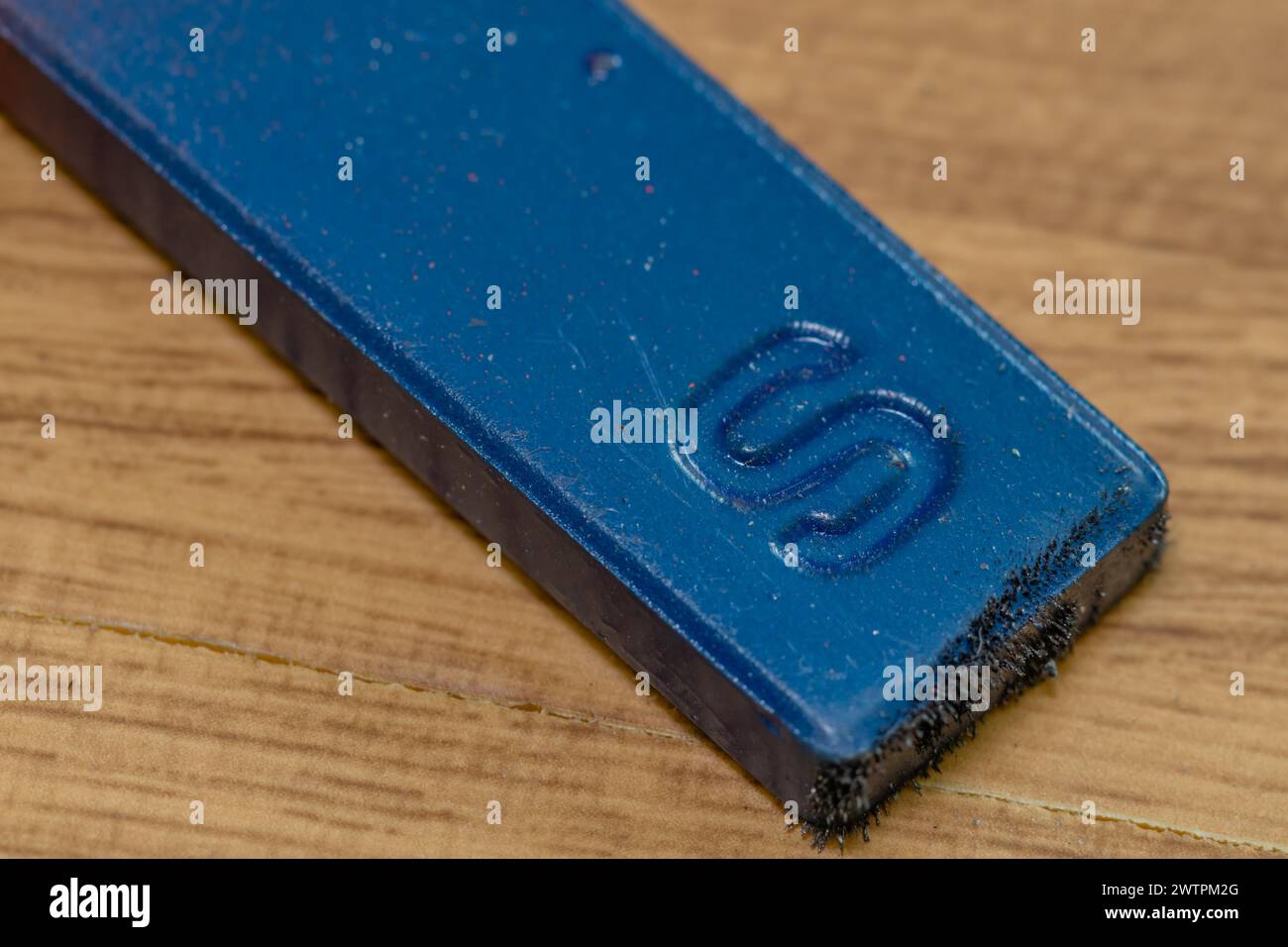 Gros plan de l'extrémité sud de couleur bleue de l'aimant avec des limailles de fer attachées sur fond de grain de bois Banque D'Images