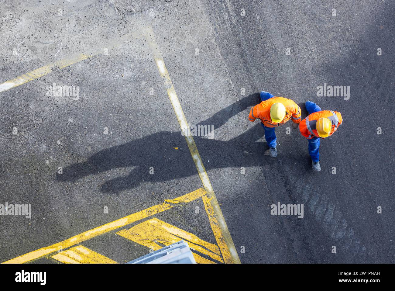 Deux ouvriers de la construction en casques de sécurité marchent sur le tarmac. Ils projettent de longues ombres. Stuttgart, Bade-Wuerttemberg, Allemagne Banque D'Images