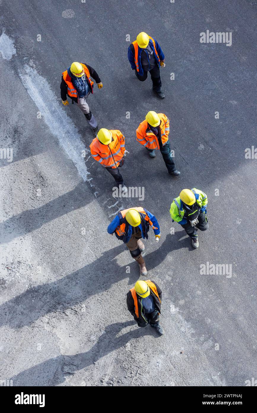 Plusieurs ouvriers de la construction portant un casque de sécurité marchent sur le tarmac. Ils projettent de longues ombres. Stuttgart, Bade-Wuerttemberg, Allemagne Banque D'Images