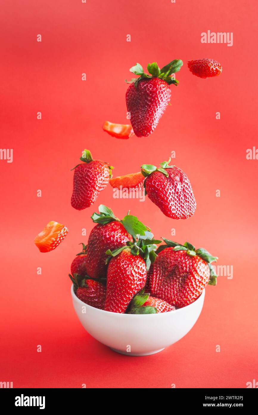 Fraises tombant sur un bol blanc. Fond rouge vif. Banque D'Images