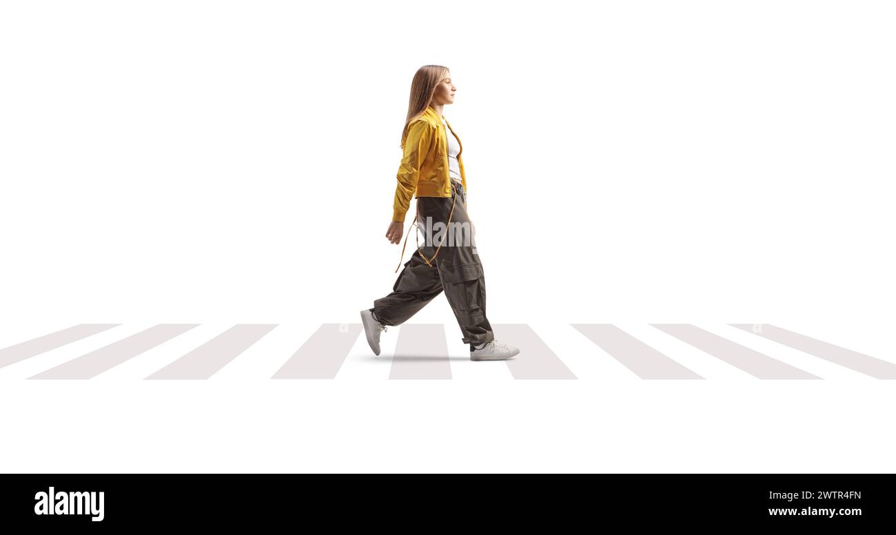 Plan de profil pleine longueur d'une adolescente à la mode marchant à un passage piétonnier isolé sur fond blanc Banque D'Images