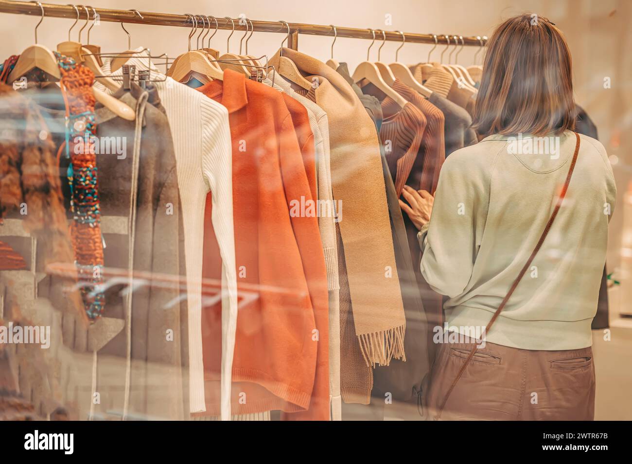 La femme fait des courses pour des vêtements dans un magasin. Elle regarde un porte-vêtements. Vue floue à travers la fenêtre du magasin, mise au point sélective Banque D'Images