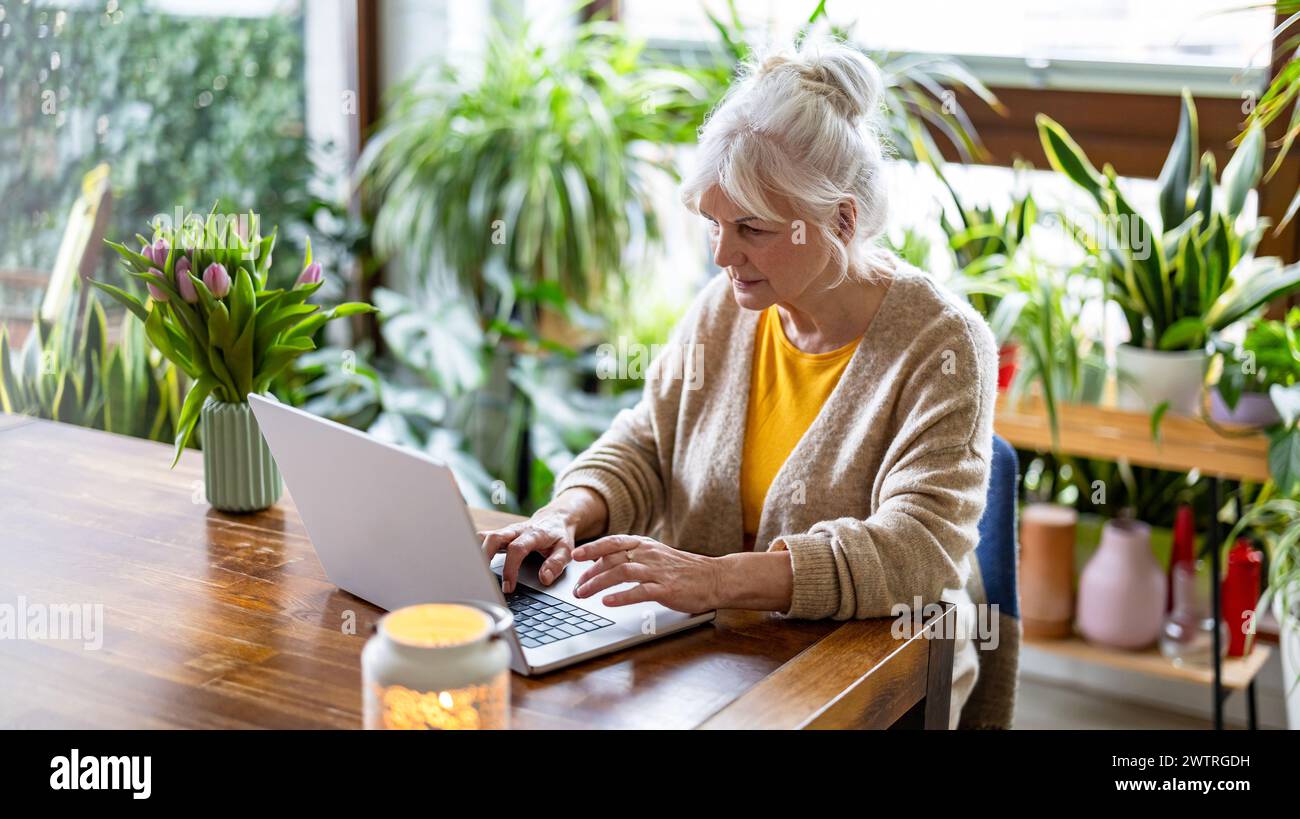 Femme mature utilisant un ordinateur portable tout en étant assis à la table à la maison Banque D'Images