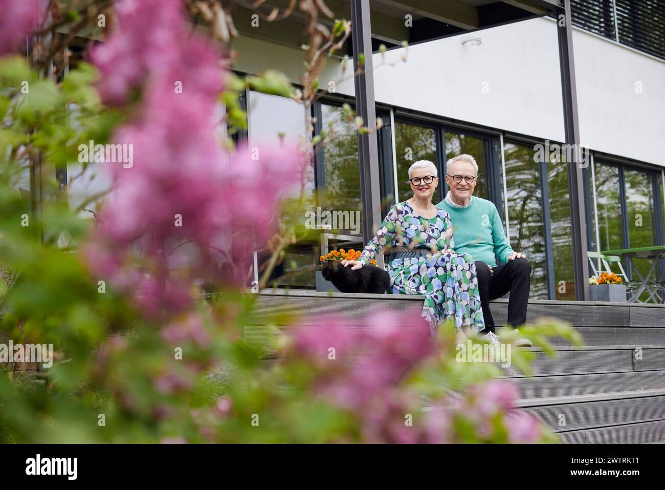 Heureux couple senior assis sur des marches devant leur maison Banque D'Images