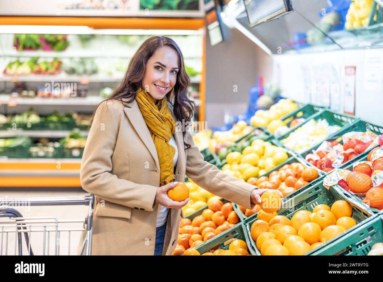 Femme magasinant pour l'épicerie avec un panier. Une jeune brune achète des fruits dans un supermarché. Banque D'Images