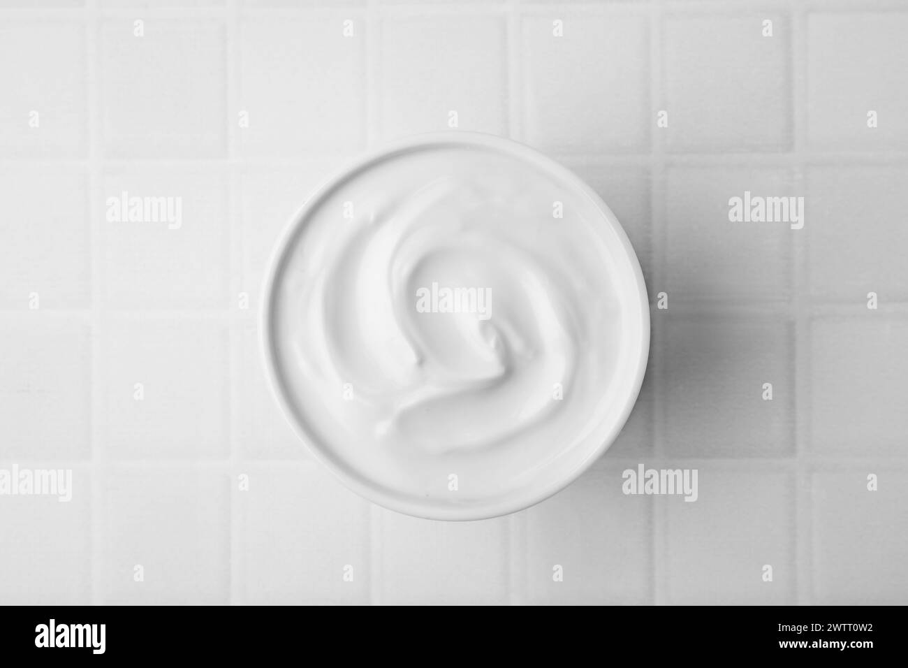 Délicieux yaourt naturel dans un bol sur une table carrelée blanche, vue de dessus Banque D'Images