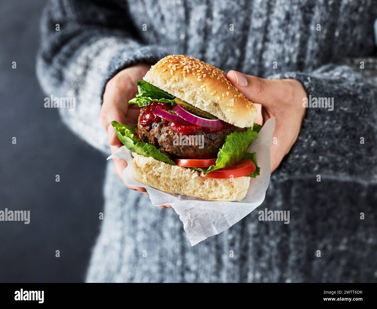 Gros plan des mains tenant un hamburger juteux prêt à manger. Banque D'Images