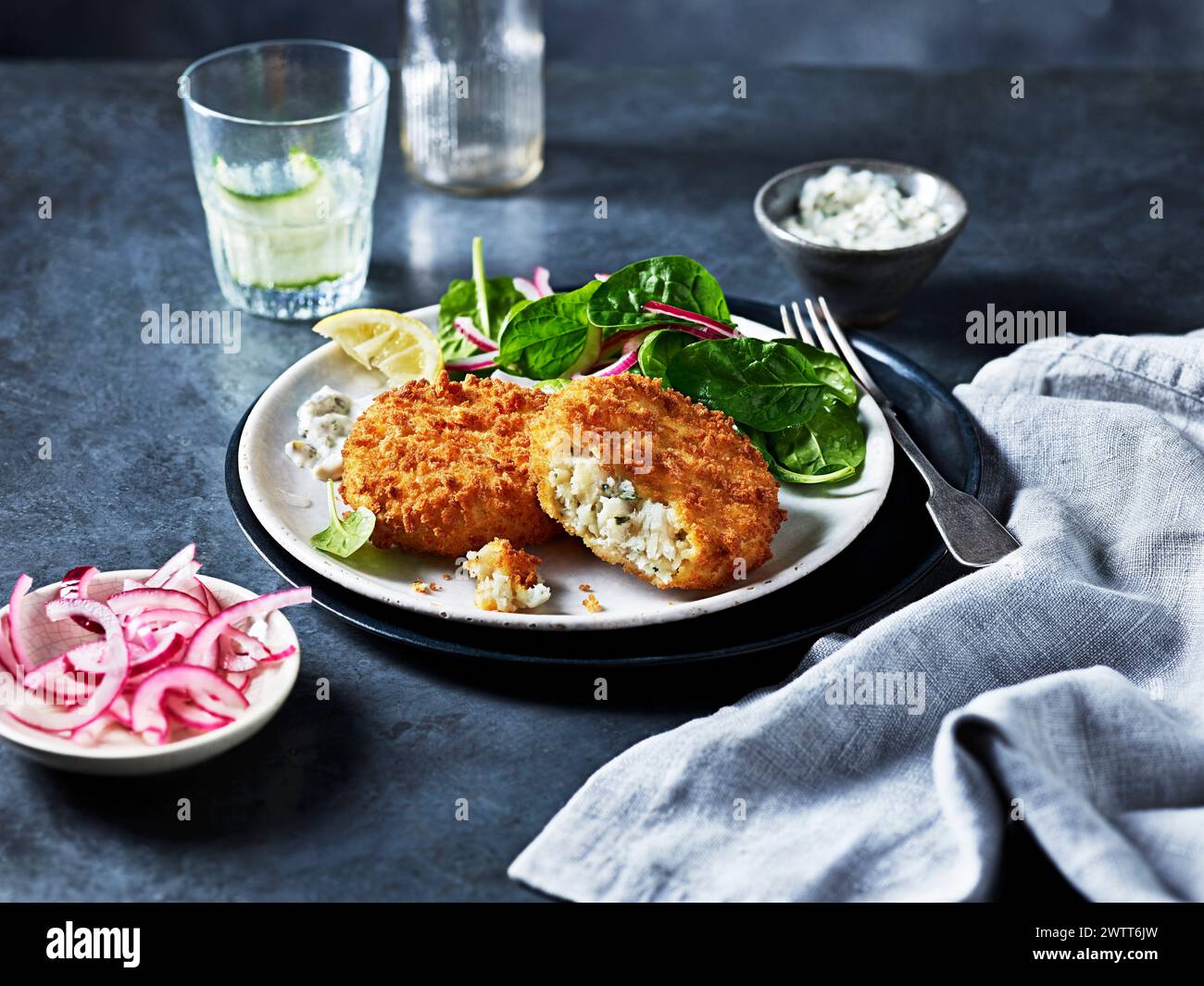 Poisson pané croustillant accompagné d'une salade d'épinards frais et d'oignons marinés tranchés sur une table sombre et élégante. Banque D'Images