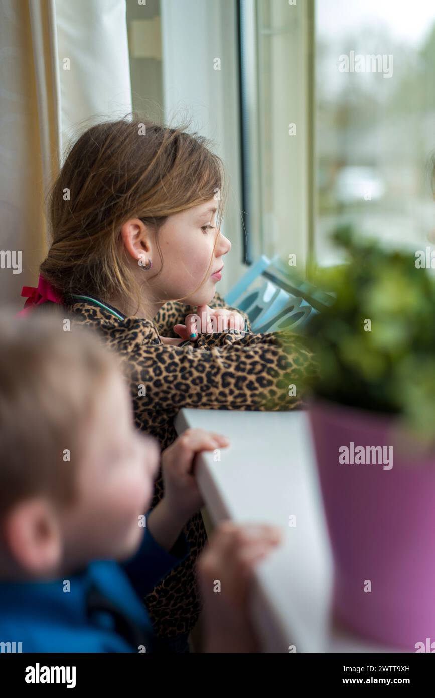 Enfant attentionné regardant par une fenêtre avec frère et sœur à proximité Banque D'Images