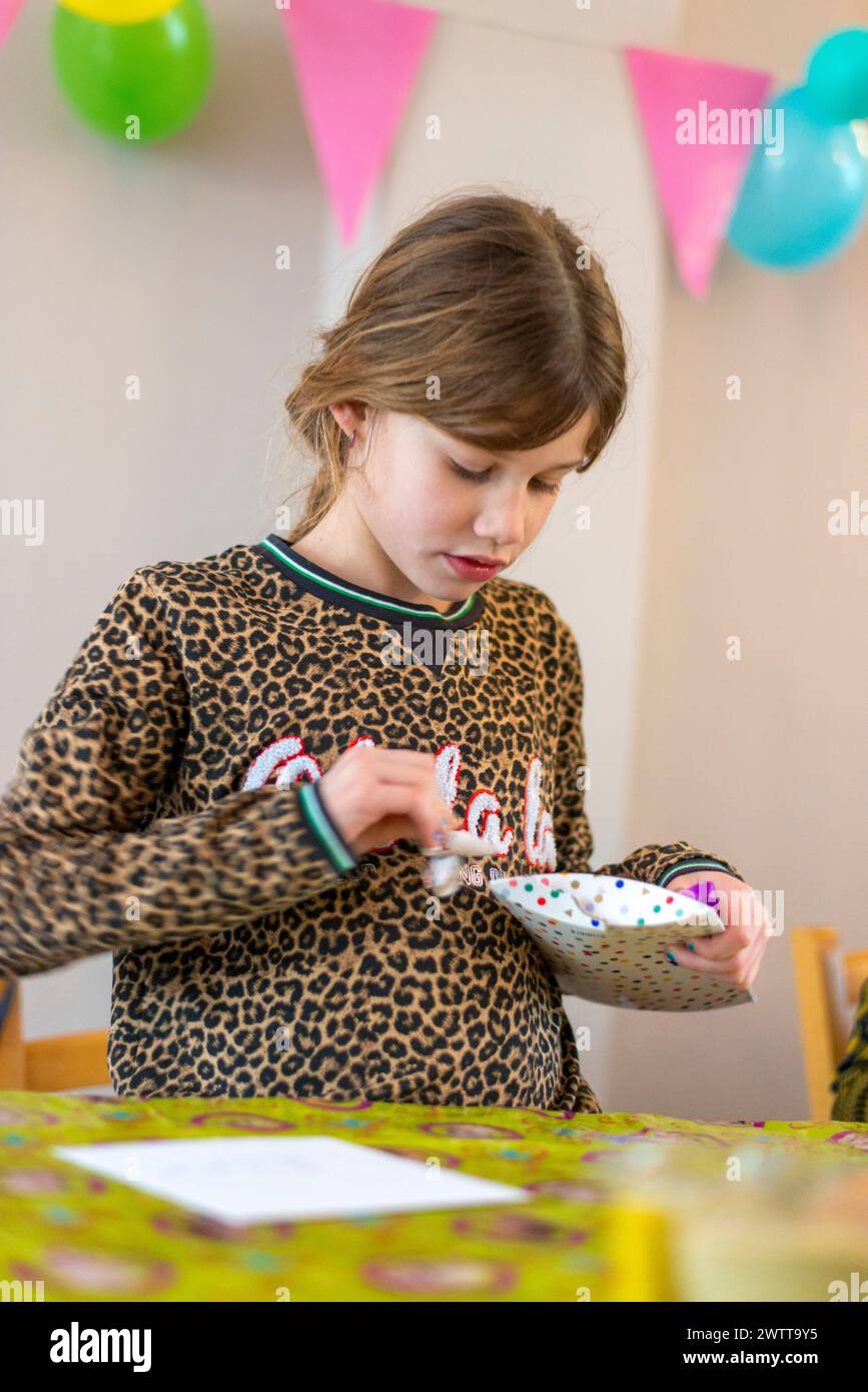 Jeune fille allumant soigneusement des bougies d'anniversaire sur un gâteau à la maison. Banque D'Images