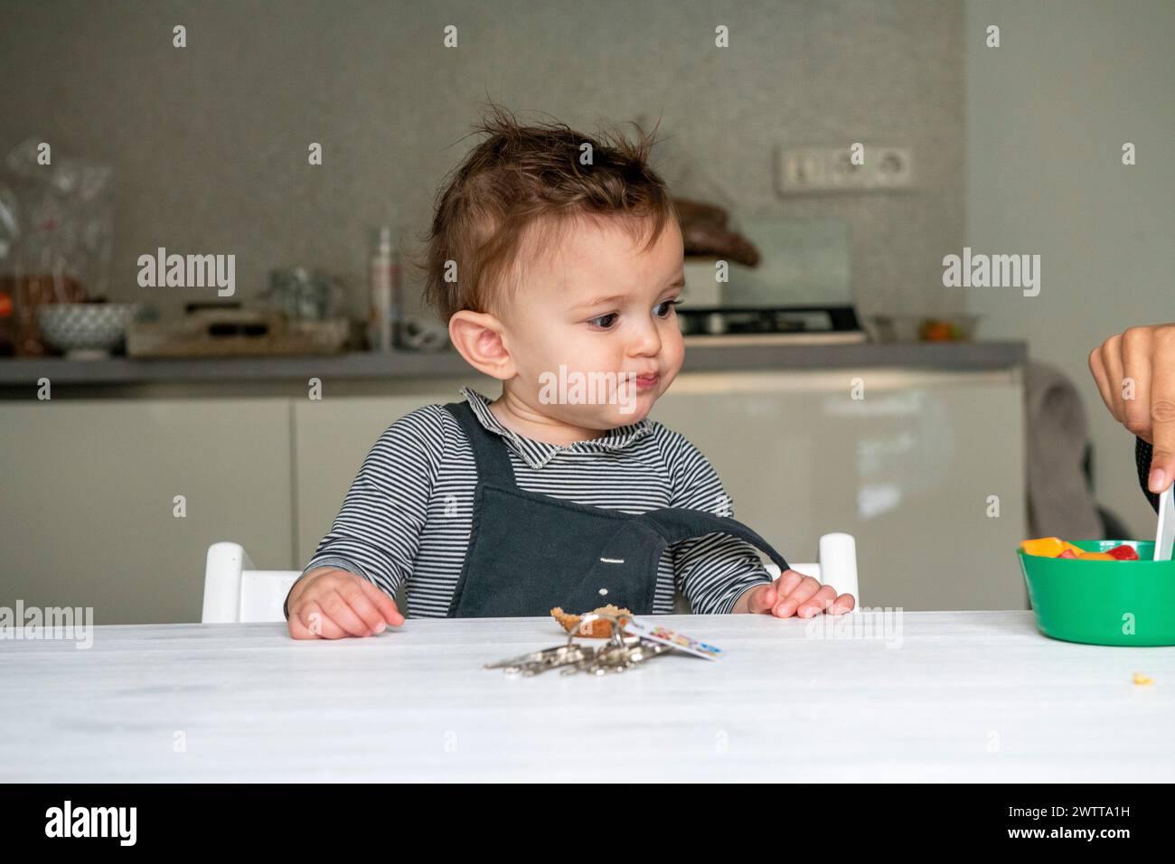 Petit bambin avec un regard curieux à la table du dîner Banque D'Images