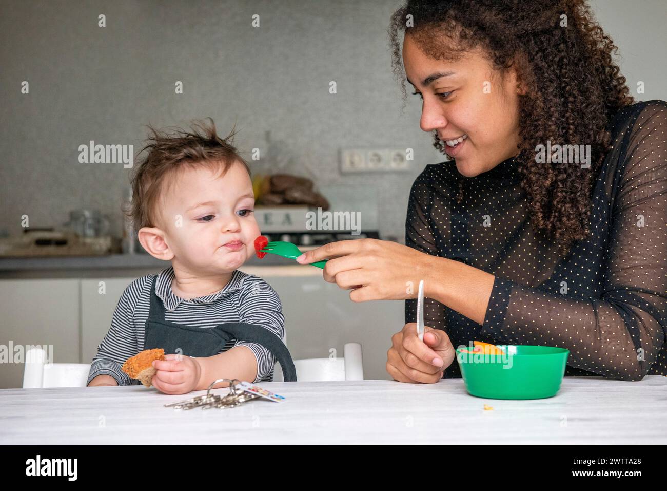 Une mère offrant doucement de la nourriture à son tout-petit à la table à manger. Banque D'Images