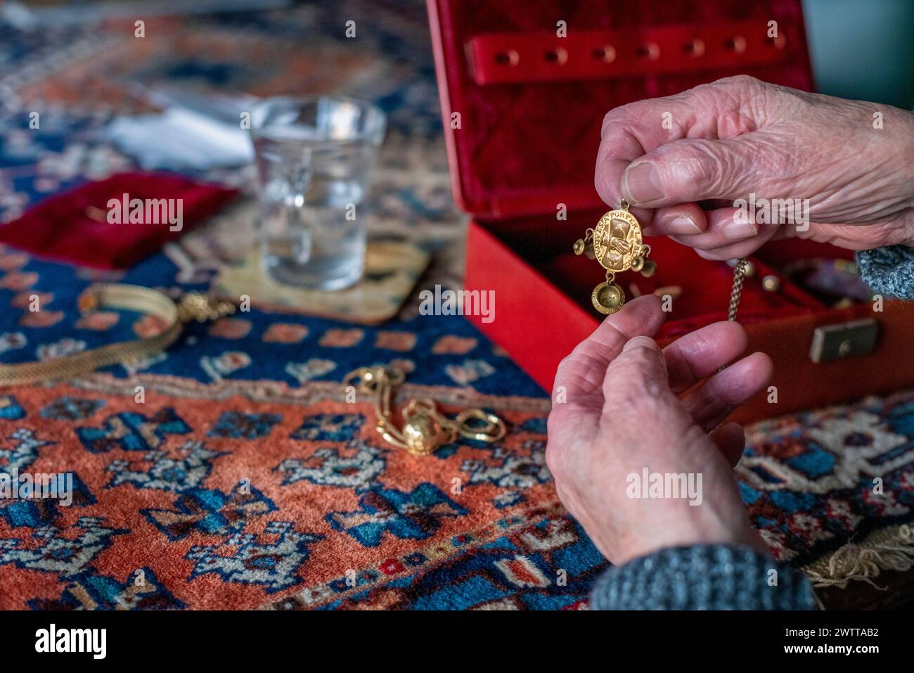 Mains âgées tenant un pendentif doré au-dessus d'une boîte à bijoux vibrante. Banque D'Images