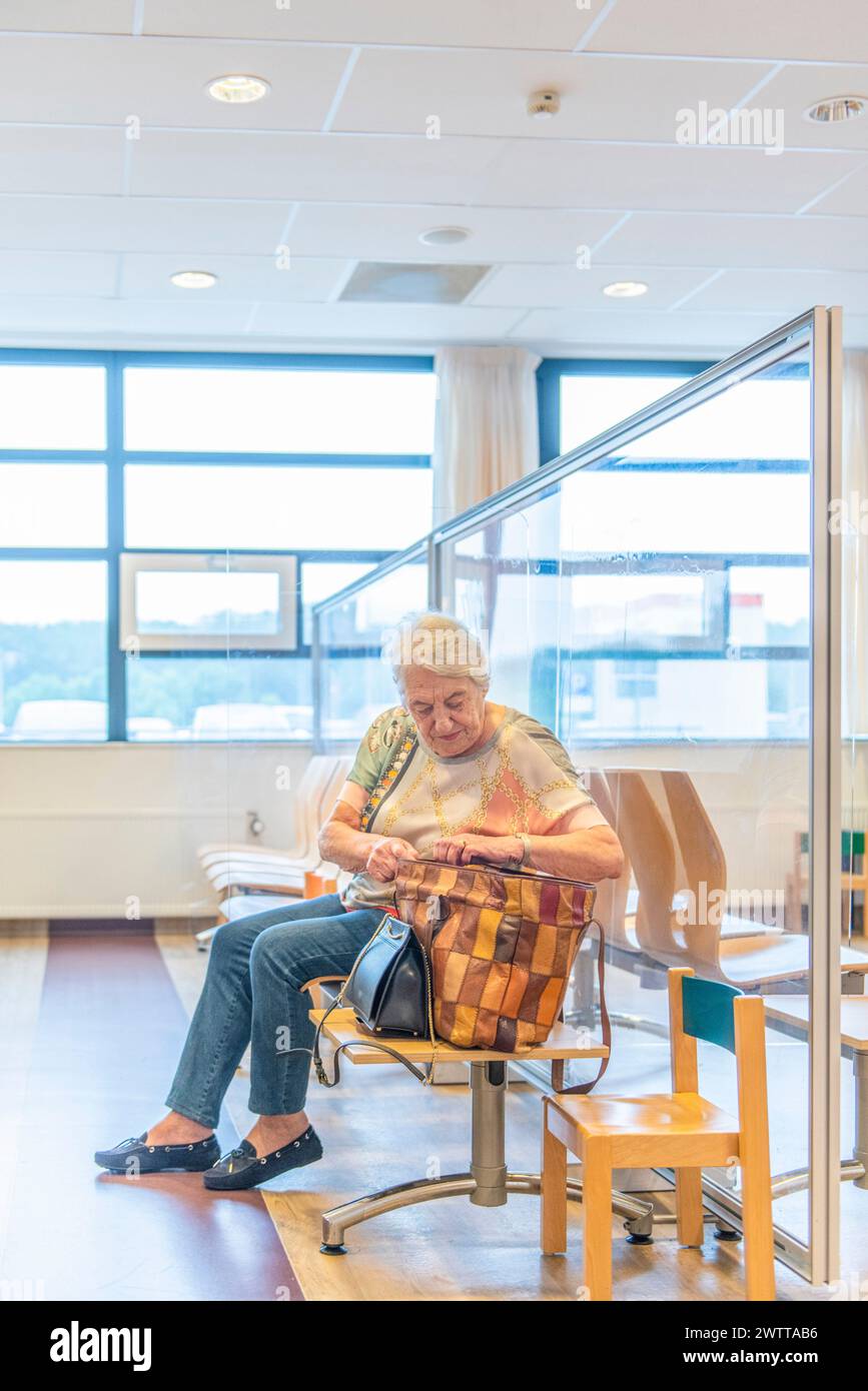 Une femme âgée assise sur une chaise dans une pièce intérieure bien éclairée, paraissant concentrée alors qu'elle tricote à partir d'un fil coloré. Banque D'Images