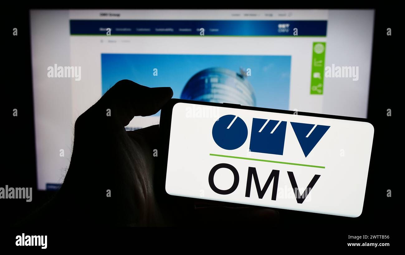 Personne tenant le téléphone portable avec le logo de la compagnie autrichienne de pétrole et de gaz OMV Aktiengesellschaft en face de la page Web de l'entreprise. Concentrez-vous sur l'affichage du téléphone. Banque D'Images