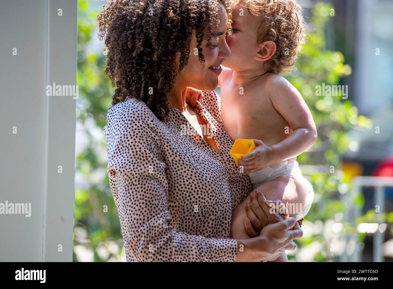 Enfant en bas âge donnant un baiser à une femme souriante par une journée ensoleillée Banque D'Images
