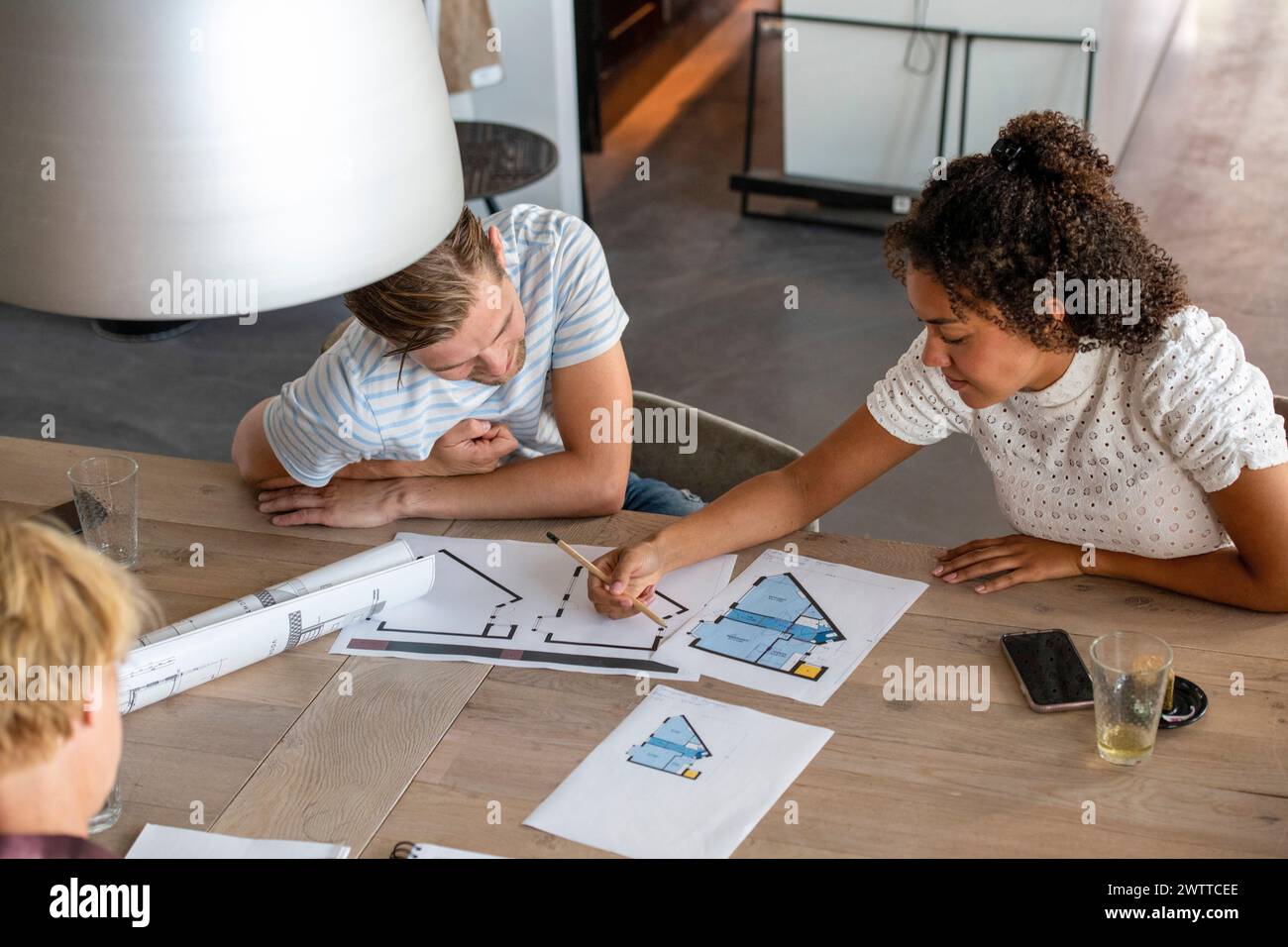 Deux personnes travaillant en collaboration sur des plans architecturaux dans un espace de travail moderne. Banque D'Images