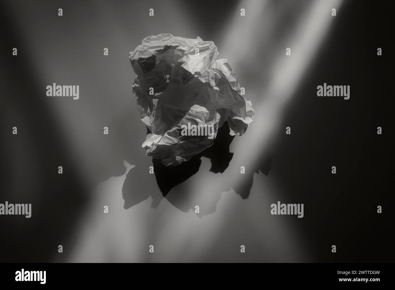 Un morceau de papier froissé suspendu dans un vide, avec la lumière projetant des ombres dramatiques Banque D'Images