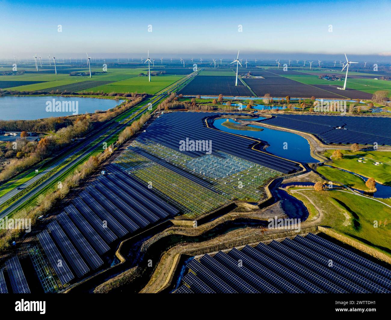 Vue aérienne d'une vaste ferme solaire à côté d'éoliennes dans un paysage verdoyant. Banque D'Images