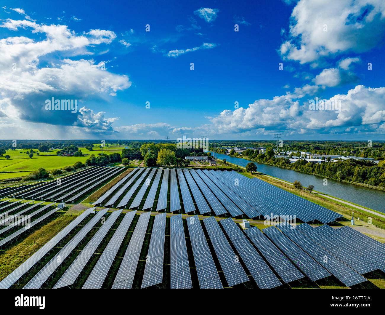 Une vue panoramique sur une ferme solaire adjacente à une rivière sous le vaste ciel nuageux. Banque D'Images