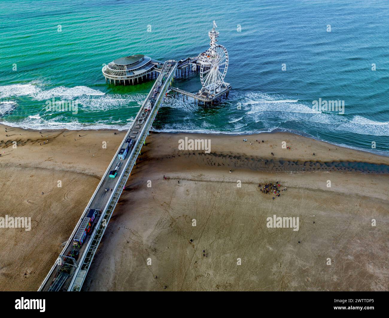 Vue aérienne d'une jetée animée s'étendant dans la mer avec des attractions et des amateurs de plage ci-dessous. Banque D'Images