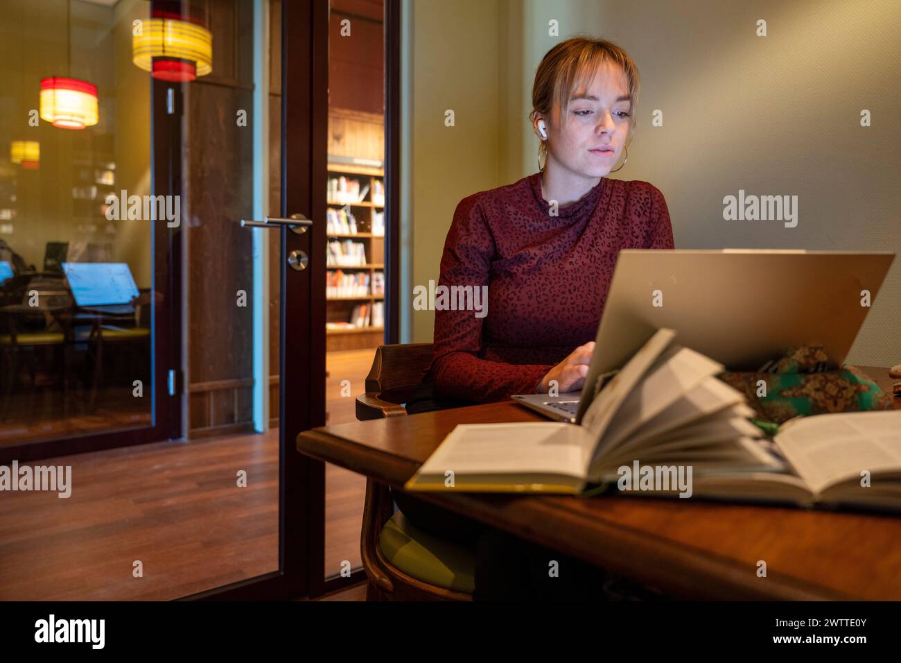 Individu concentré étudiant dans un coin bibliothèque confortable avec un ordinateur portable et des livres. Banque D'Images