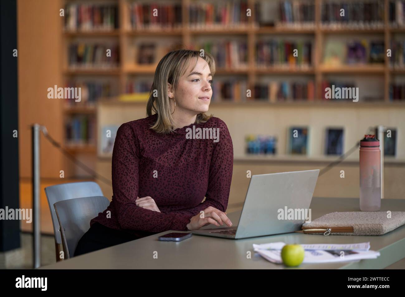 Femme concentrée travaillant sur son ordinateur portable dans un cadre de bibliothèque. Banque D'Images