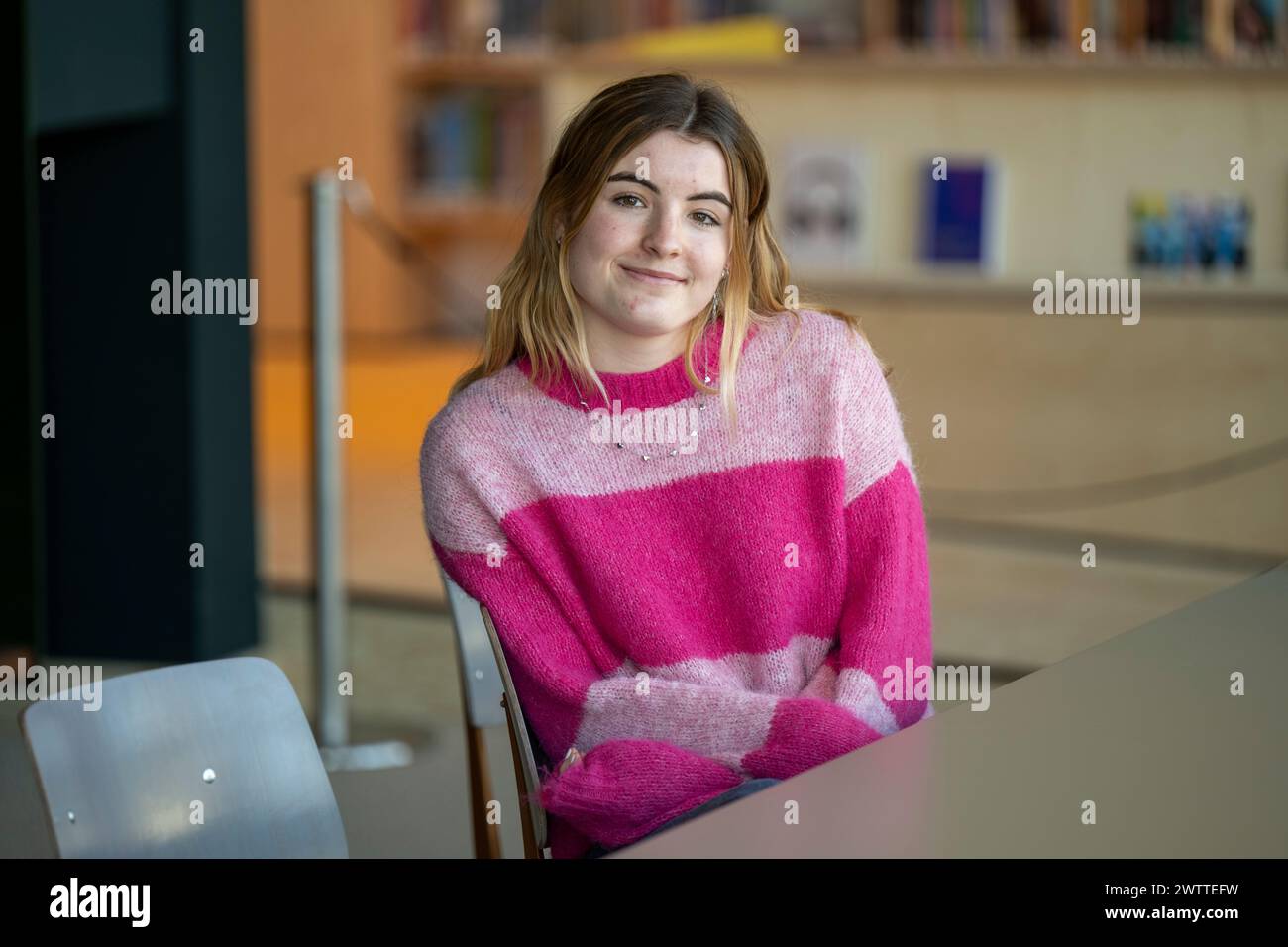 Jeune femme souriant à la caméra dans un cadre de bibliothèque. Banque D'Images