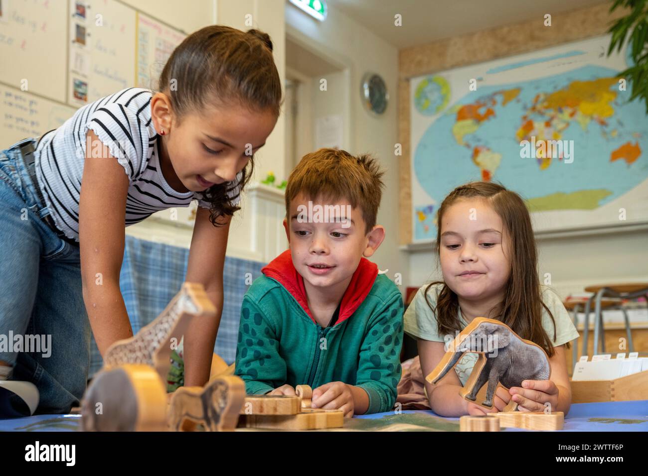 Enfants curieux s'engageant avec des jouets d'animaux en bois dans un cadre de classe. Banque D'Images