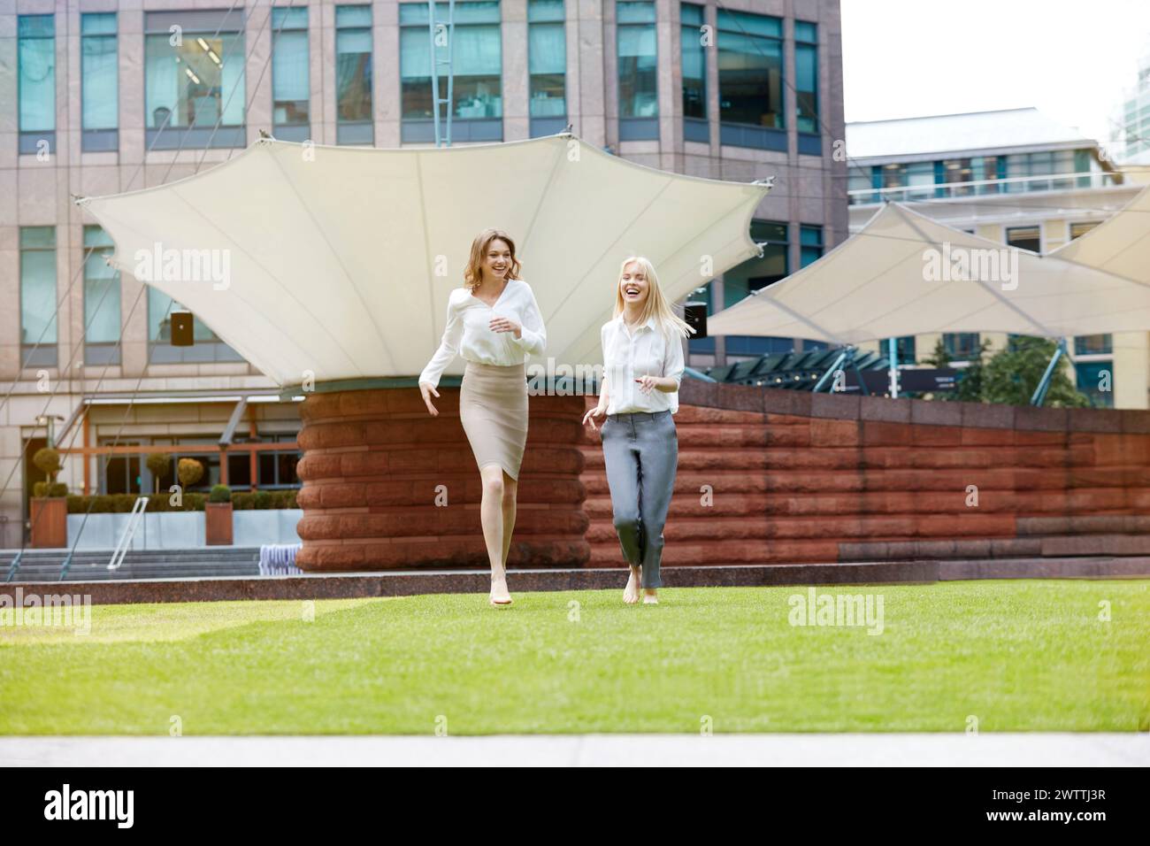 Deux femmes qui courent joyeusement sur l'herbe en milieu urbain Banque D'Images