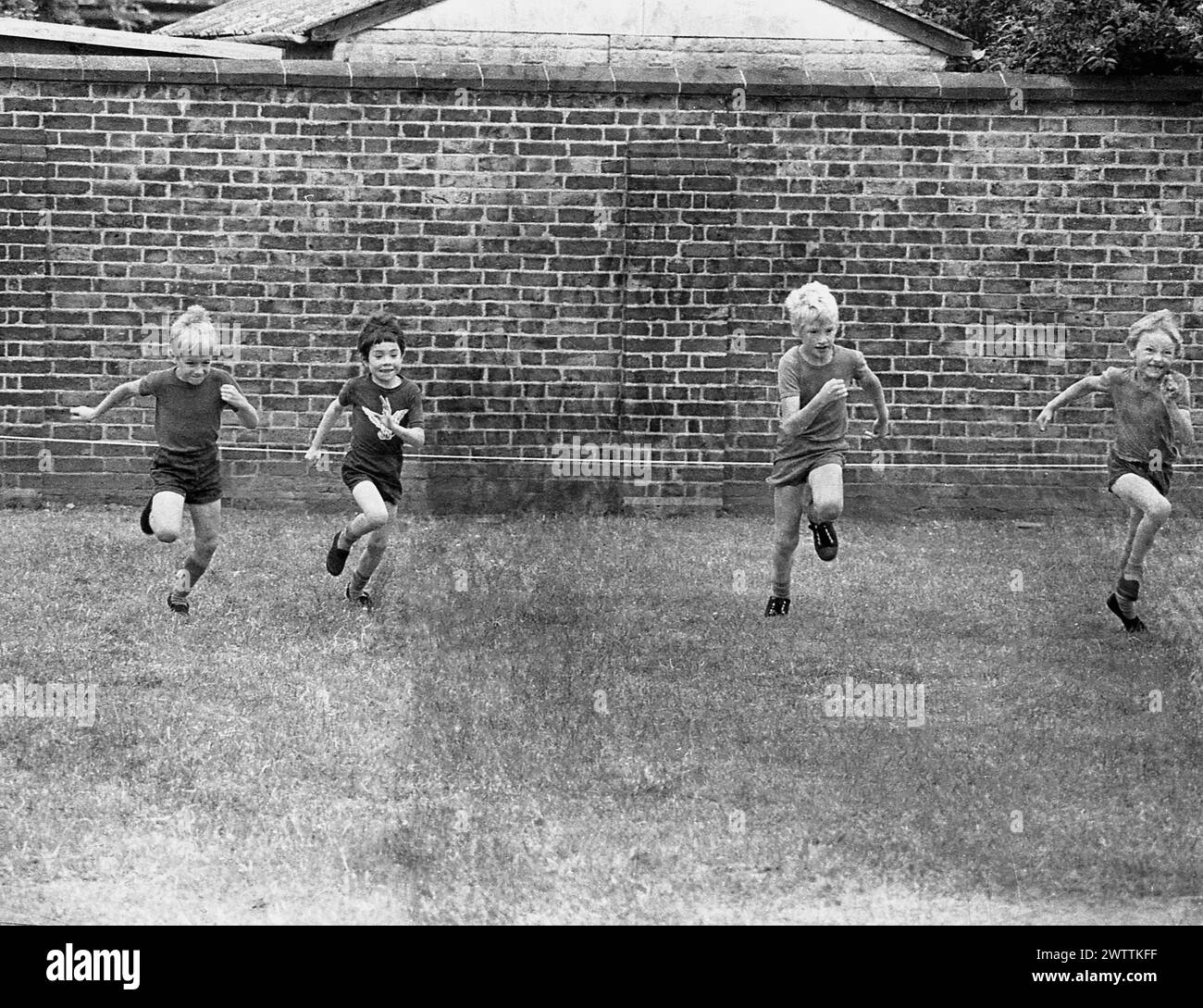 Années 1960, historique, quatre écoliers du primaire prenant part à une course de sprint sur herbe dans un champ clos, Angleterre, Royaume-Uni. Banque D'Images