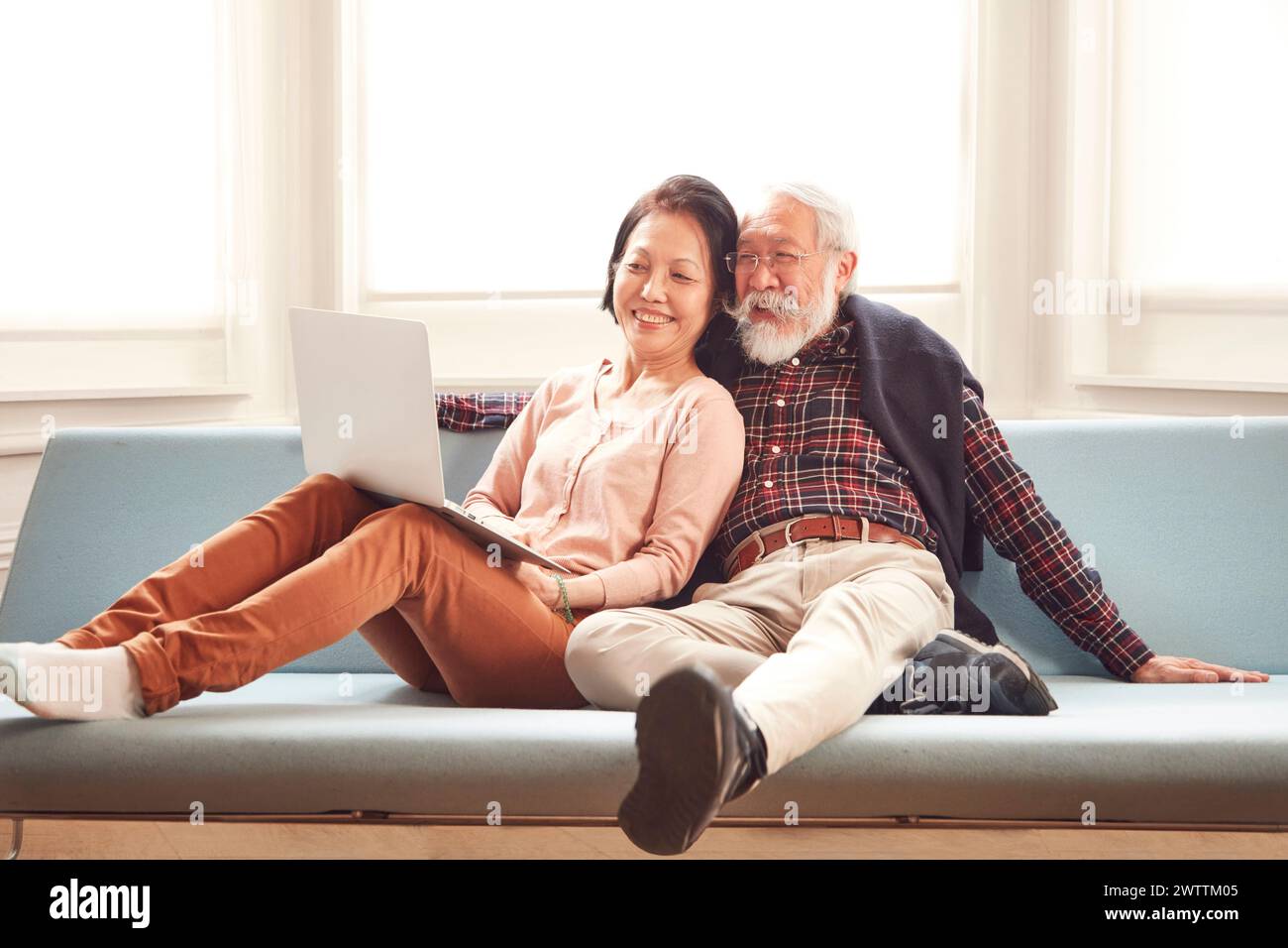 Couple de personnes âgées se relaxant sur un canapé avec un ordinateur portable Banque D'Images