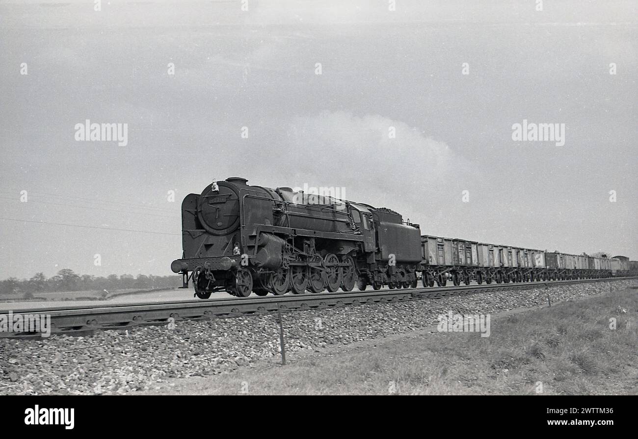 Années 1960, historique, une locomotive à vapeur British Railway 92216, sur voie ferrée tirant des wagons de fret, Angleterre, Royaume-Uni. Avec un design distinctif, les locomotives à vapeur BR Class 9F ont été utilisées pour tirer de lourds wagons de marchandises, à grande vitesse, sur de longues distances, mais ont également été utilisées sur les trains de voyageurs. La dernière locomotive à vapeur construite par British Railways en 1960 était une classe 9F, la 92220 Evening Star. Banque D'Images