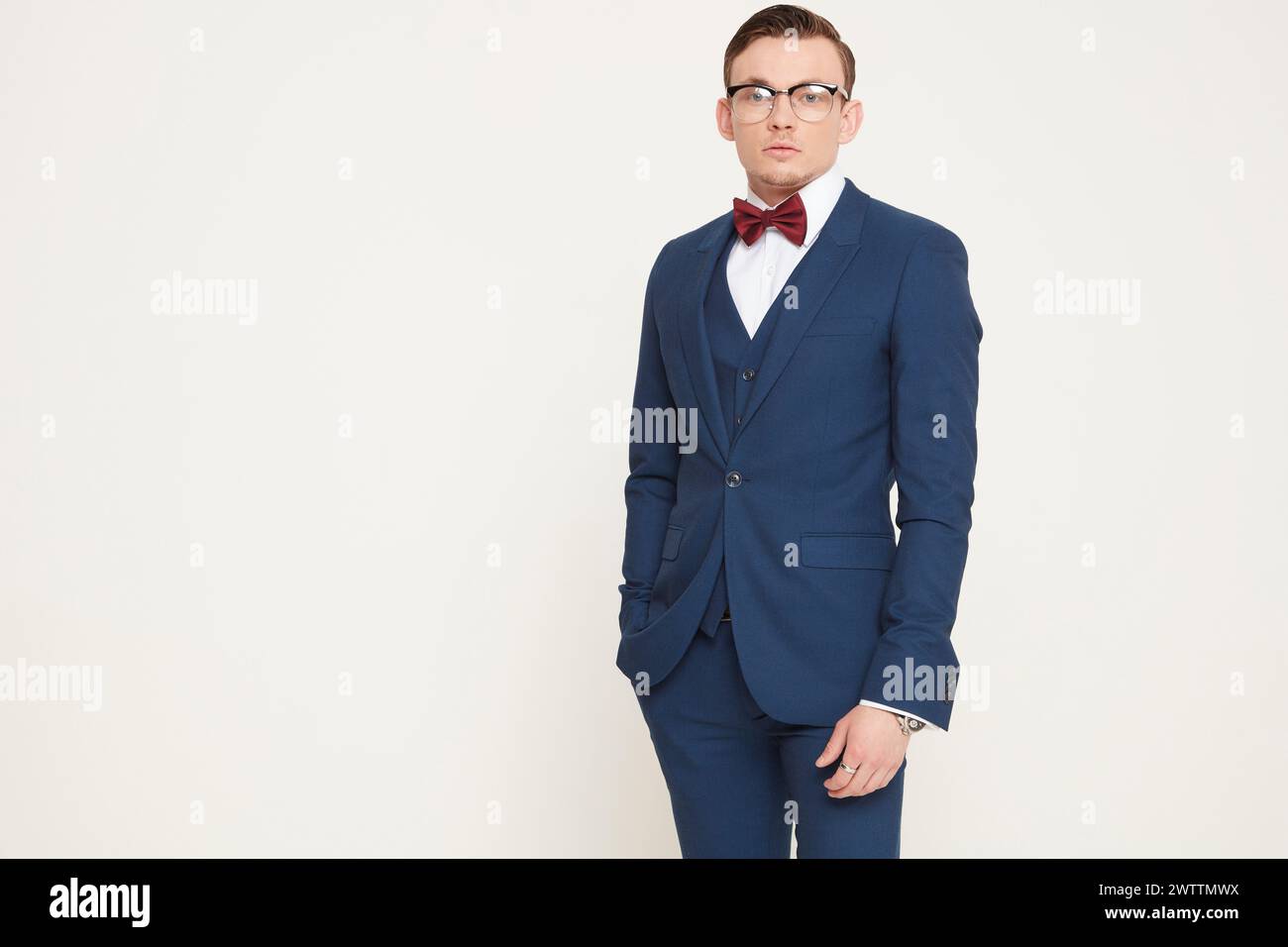 Homme en costume bleu et noeud papillon rouge sur un fond crème Banque D'Images