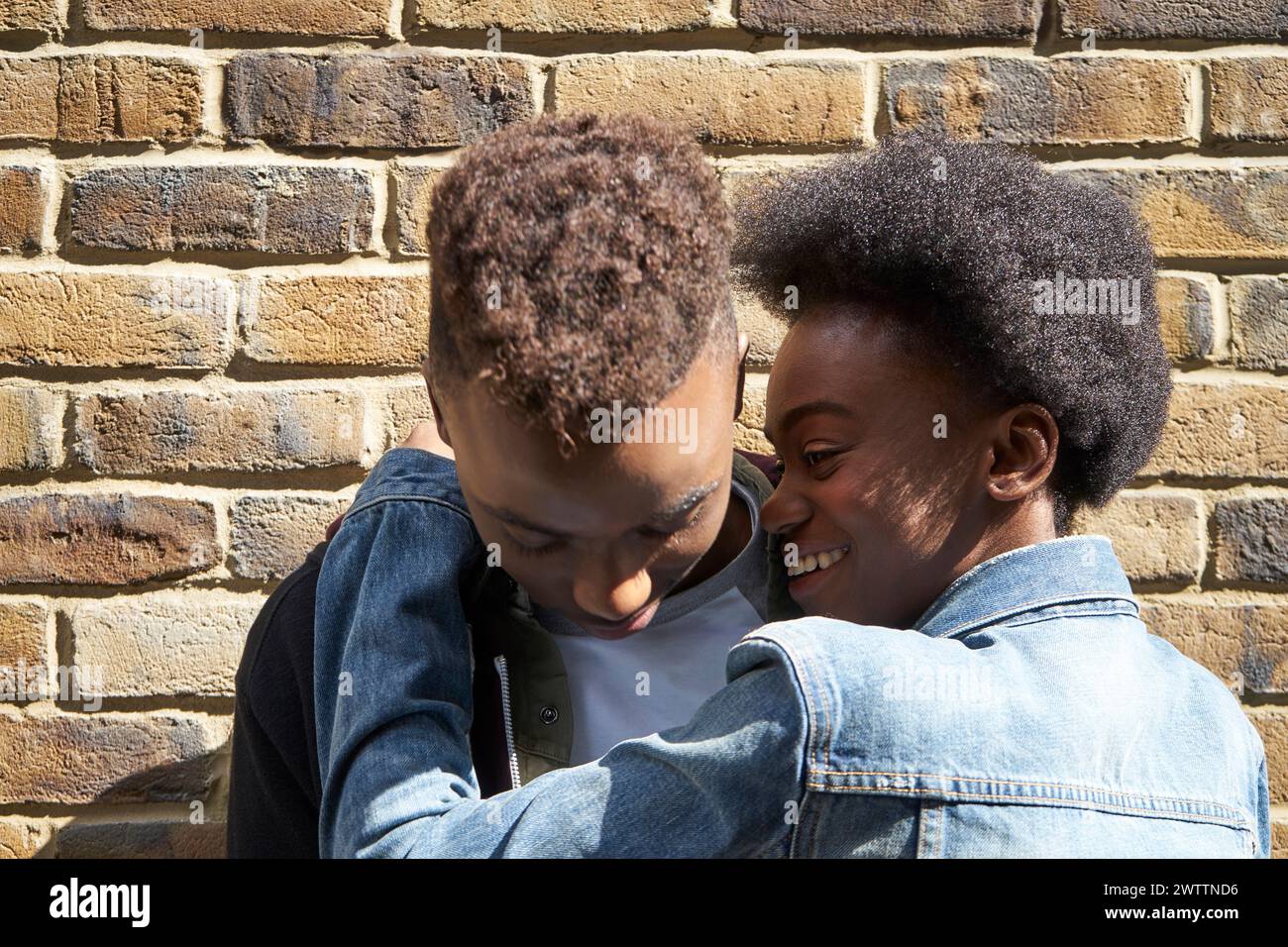 Deux personnes souriant et s'embrassant contre un mur de briques Banque D'Images Deux personnes souriant et s'embrassant contre un mur de briques Banque D'Images