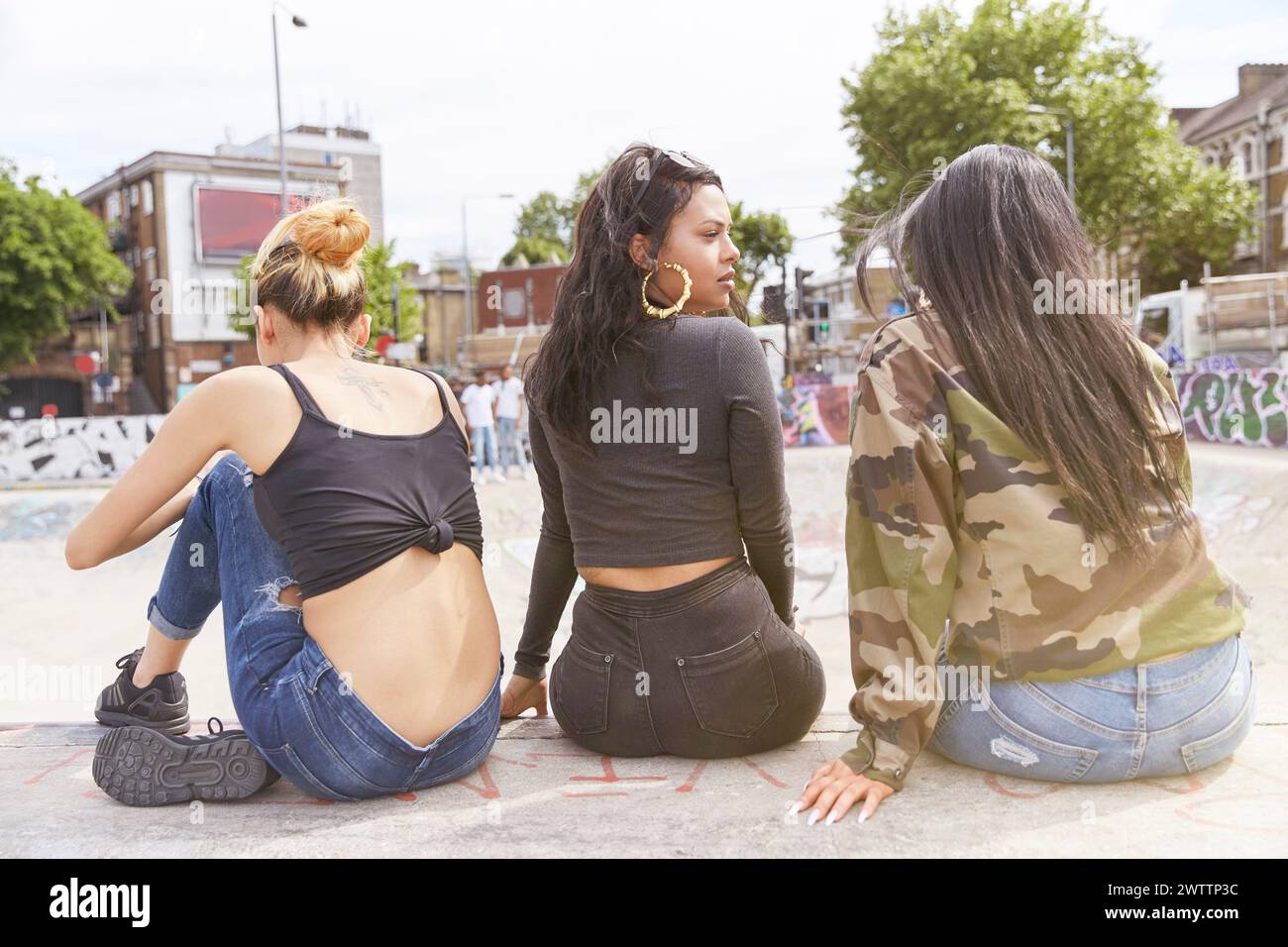 Trois femmes assises à l'extérieur près d'un skatepark Banque D'Images