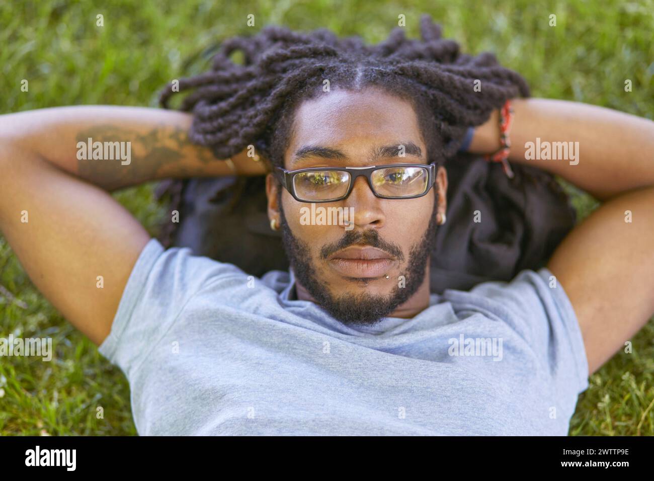 Homme se relaxant sur l'herbe avec les mains derrière la tête Banque D'Images