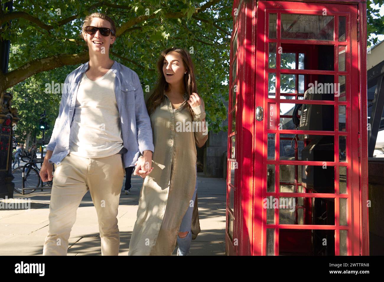 Deux personnes se promenant devant une cabine téléphonique rouge Banque D'Images