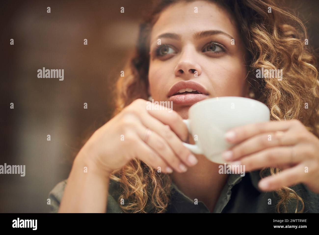 Femme sirotant d'une tasse, perdue dans ses pensées. Banque D'Images