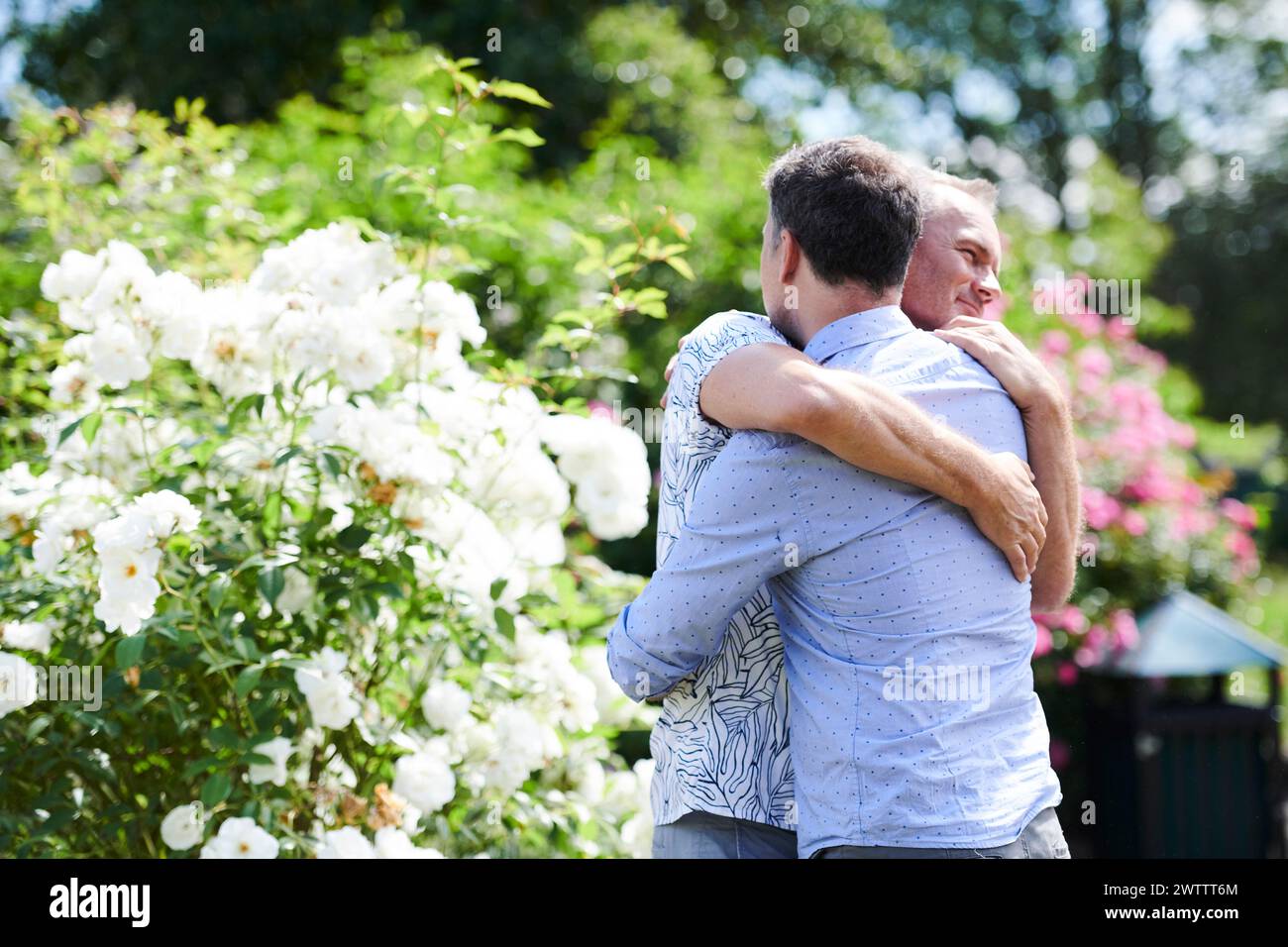 Deux hommes embrassant dans un jardin avec des fleurs blanches Banque D'Images