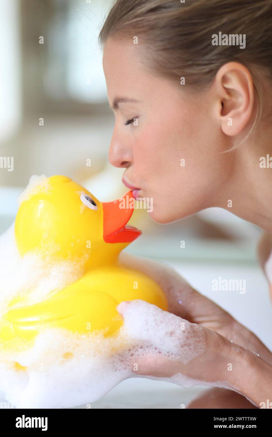 Femme embrassant un canard en caoutchouc dans un bain moussant Banque D'Images