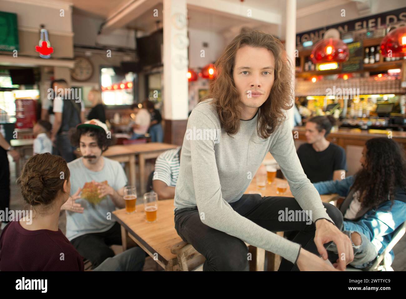 Jeune homme assis dans un bar animé Banque D'Images