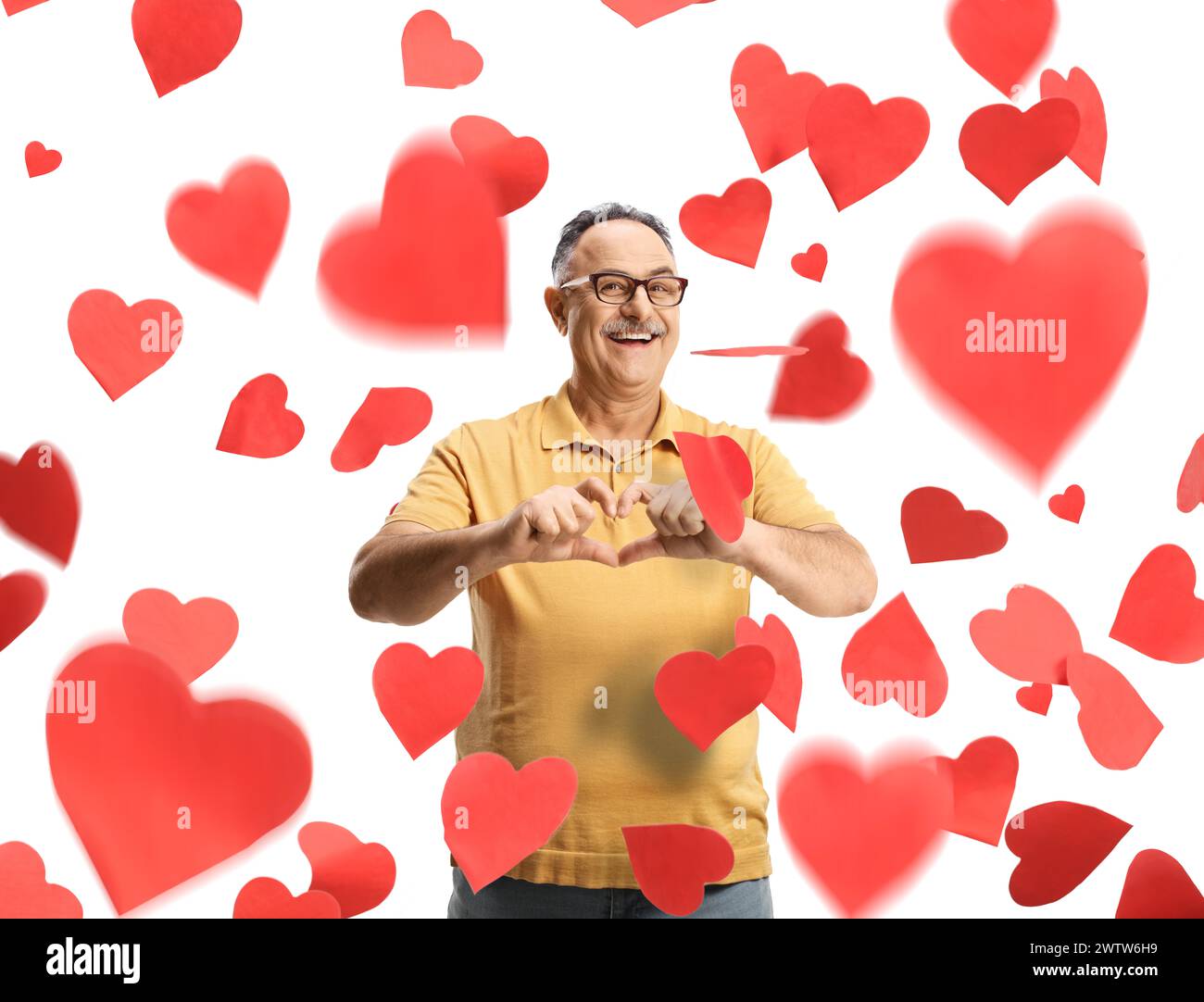 Homme mûr heureux gestionnant un symbole de cœur sous des cœurs tombants isolés sur fond blanc Banque D'Images