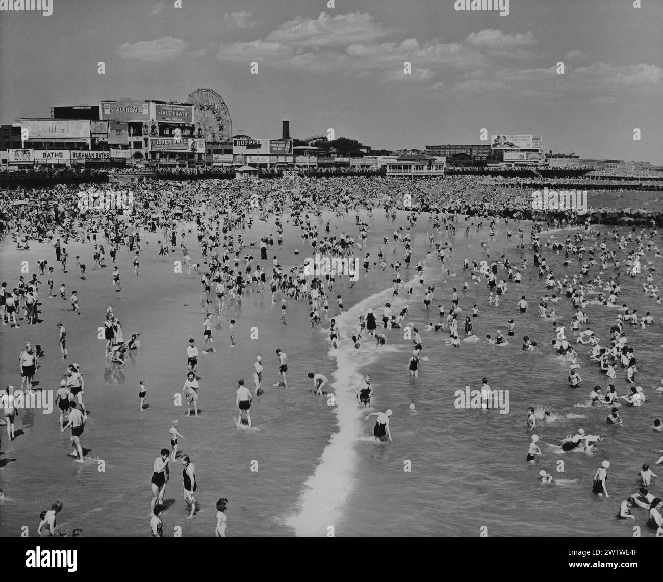 Vue surélevée le long de la côte montrant une plage bondée et l'océan à Coney Island, New York, Luna Park peut être vu en arrière-plan Banque D'Images