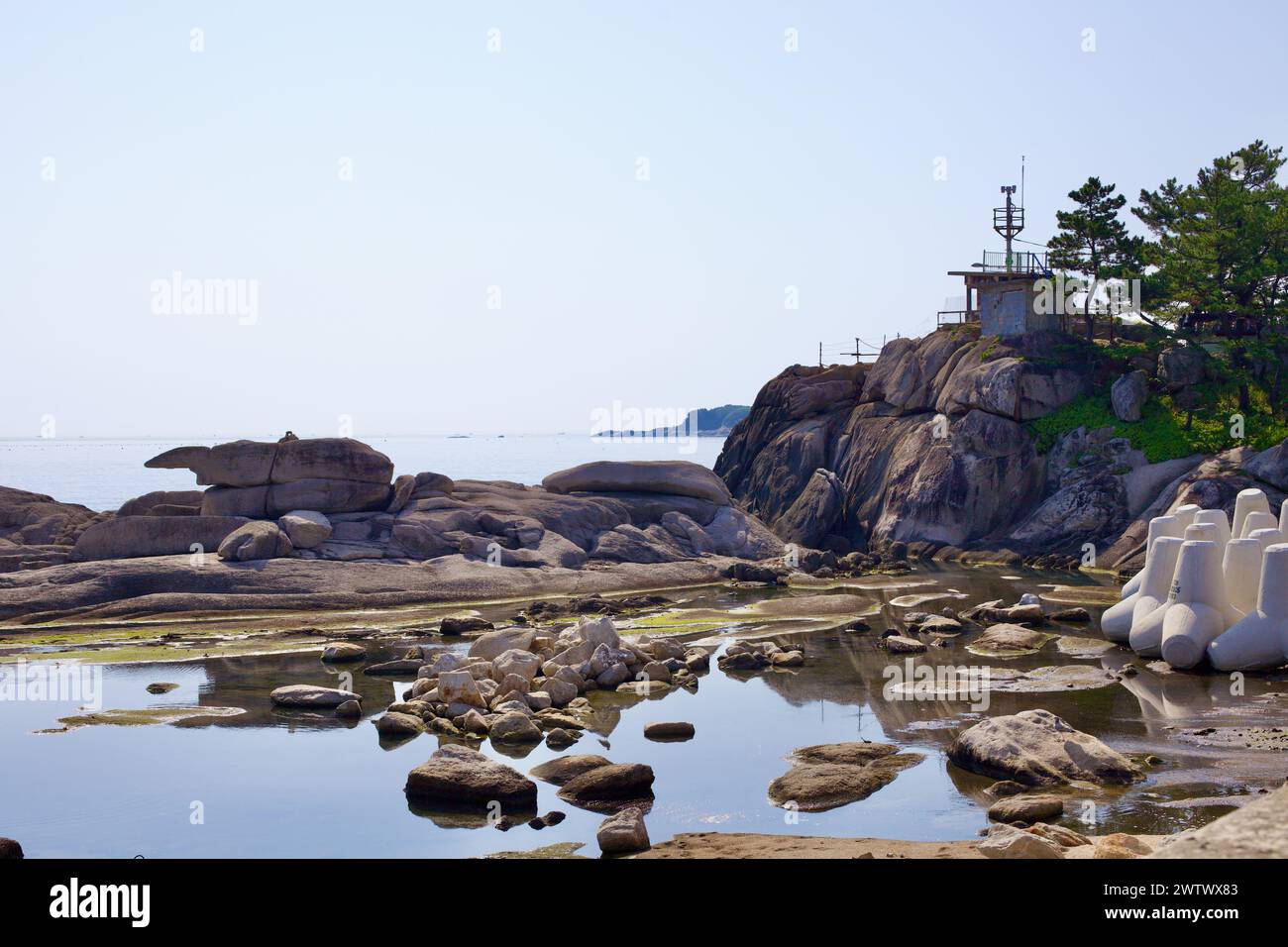 Comté de Goseong, Corée du Sud - 30 juillet 2019 : les rochers côtiers de Cheonjin Beach piègent les eaux placides de la mer de l'est, avec un belvédère militaire à la retraite pos Banque D'Images
