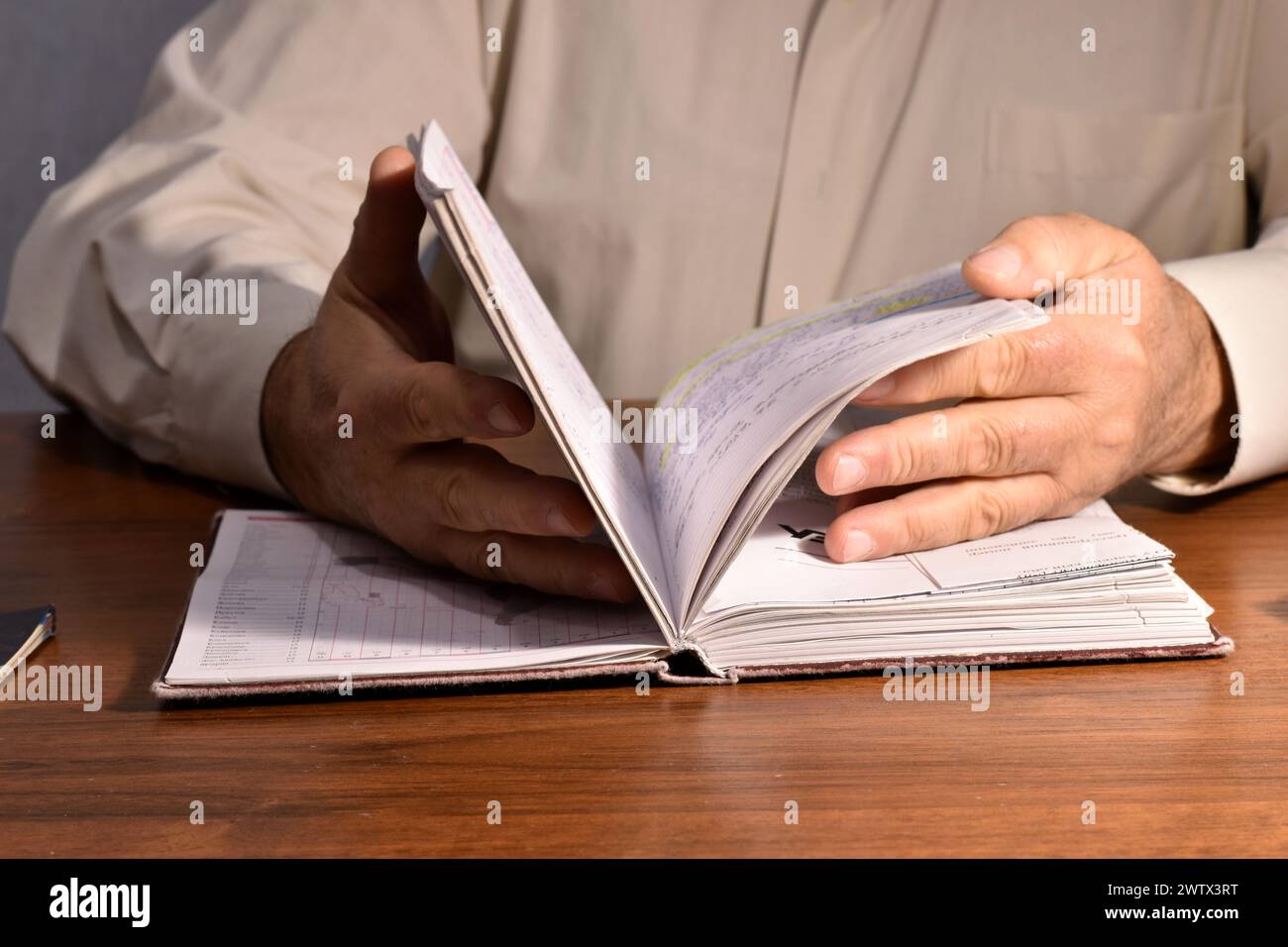 Un homme assis à une table feuillette les pages d'un cahier et lit les informations. Banque D'Images